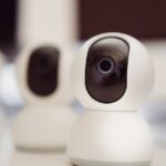 Close-up of three smart home security cameras placed on a white desk indoors.