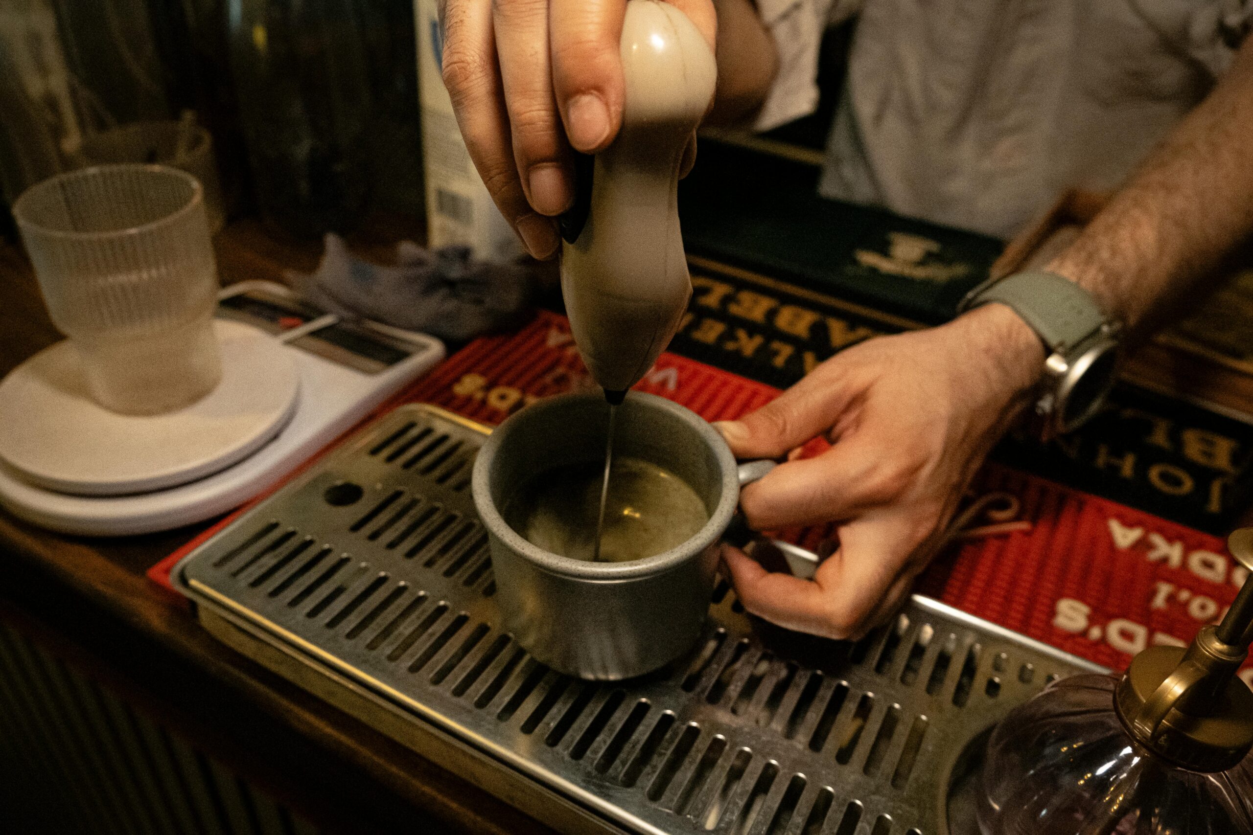 Barista using a handheld frother to make creamy coffee in an artisan cafe setting.