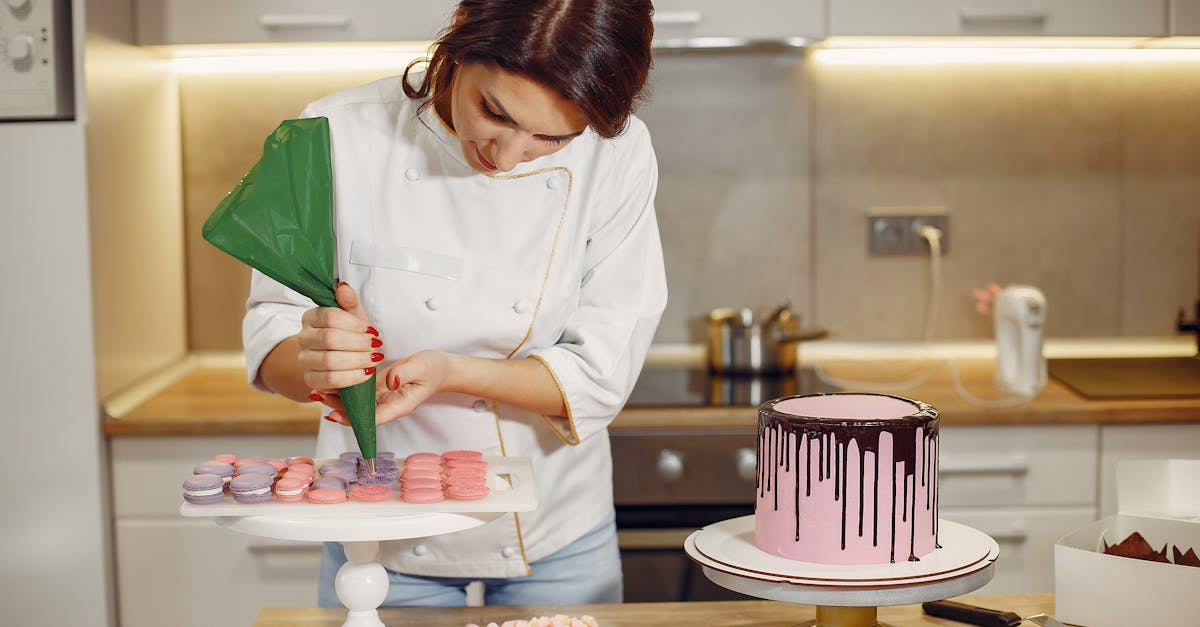 Focused young woman in uniform piping cream from pastry bag on middle of desserts after preparing delicious cake in modern cafeteria