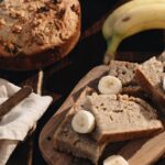 A rustic presentation of homemade banana bread with fresh bananas on a wooden board.