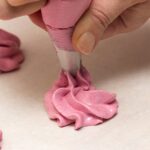 Hand piping meringue cookies with pink icing in a close-up shot.
