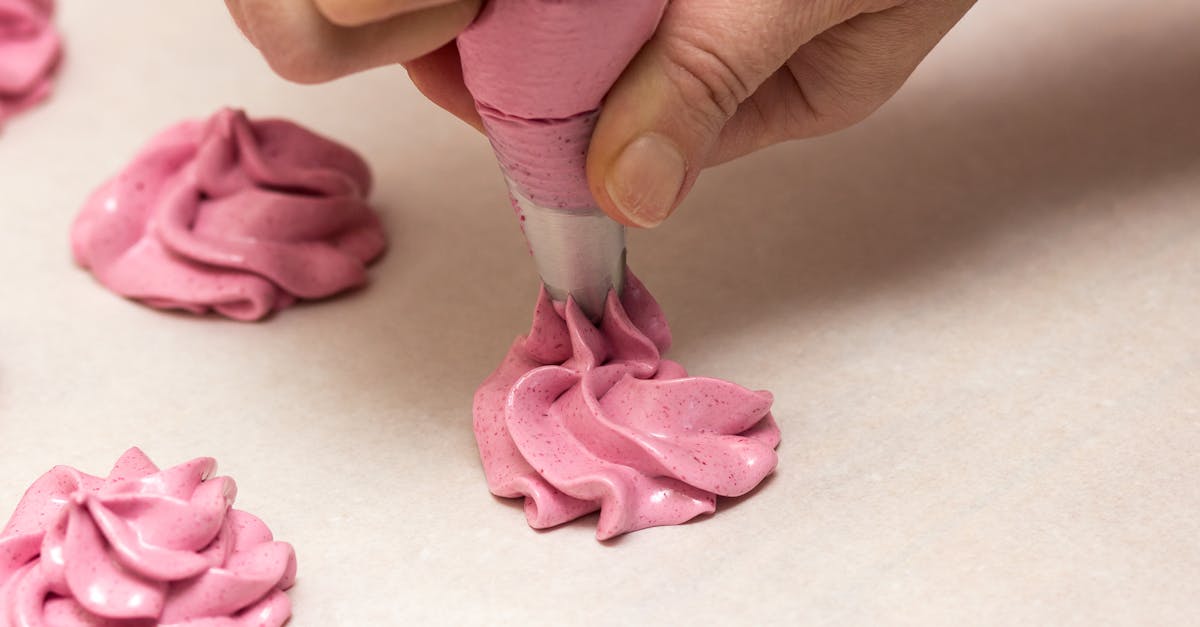 Hand piping meringue cookies with pink icing in a close-up shot.