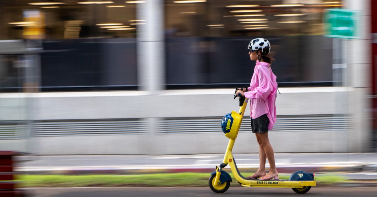 Woman in pink jacket rides a yellow electric scooter on a city street. Blurred motion effect.