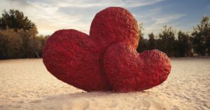Large red heart sculptures on a sandy beach at daytime, symbolizing romance and love.