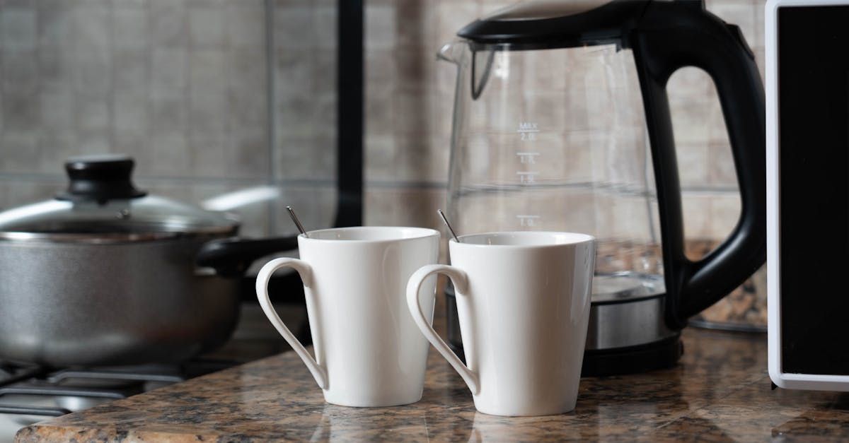 A warm indoor shot of two coffee mugs next to a kettle on a stylish kitchen counter.