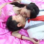 A couple in formal attire embraces on a pink blanket, enjoying a moment of affection outdoors.