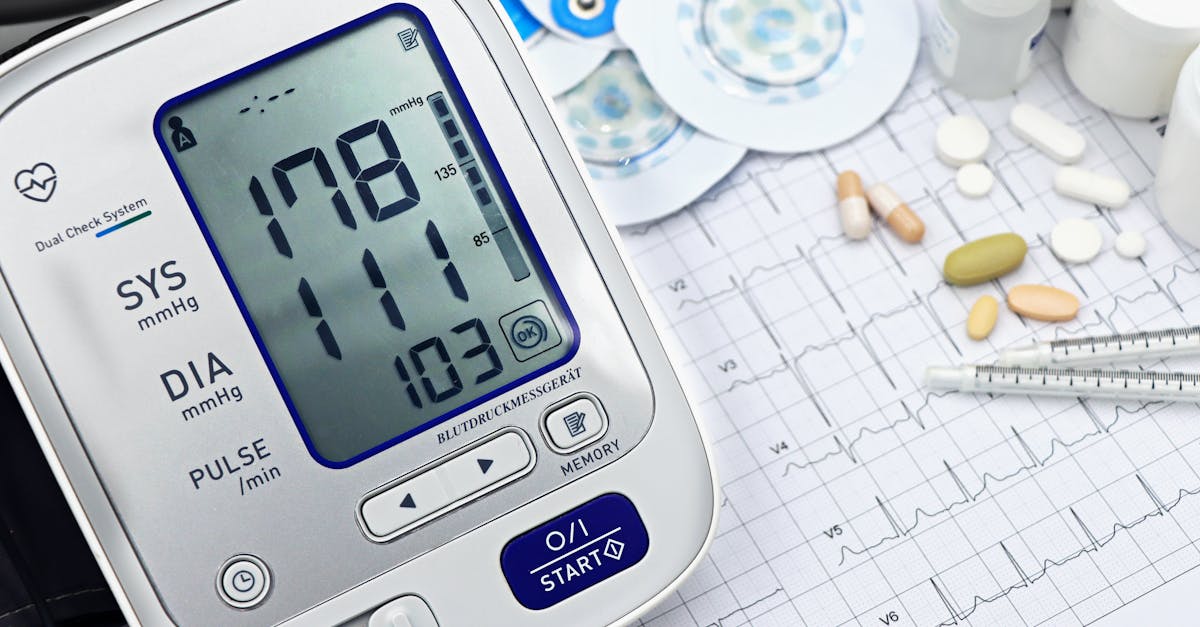 Close-up of a digital blood pressure monitor with ECG printout, pills, and medical tools.
