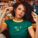 Portrait of a young woman in a vibrant setting wearing a Brazil t-shirt, seated indoors.