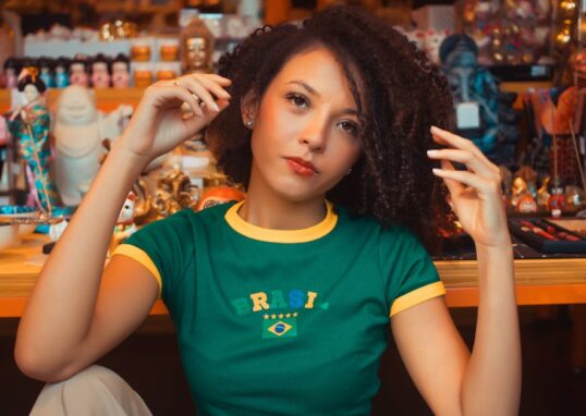Portrait of a young woman in a vibrant setting wearing a Brazil t-shirt, seated indoors.