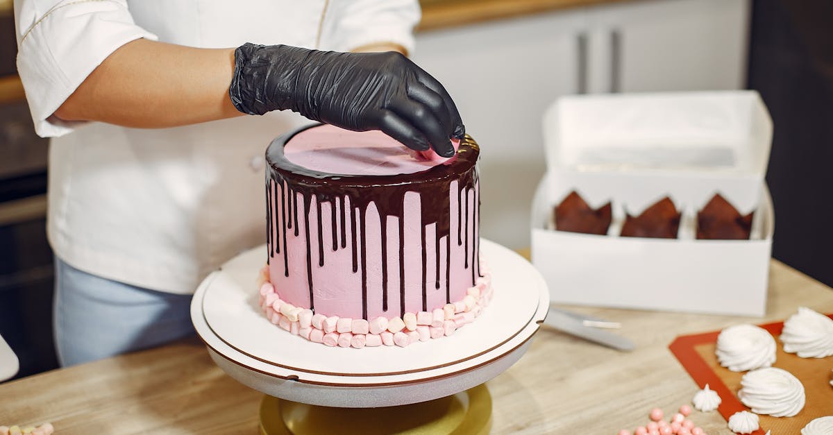 Unrecognizable female in apron and latex gloves garnishing delicious cake with sweet details while standing near table in modern restaurant