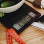 A bowl of fresh vegetables on a kitchen scale with measurement tools, depicting a healthy lifestyle.