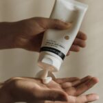 Close-up of a woman squeezing lotion onto her hand, emphasizing skincare and self-care routine.