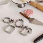 Selection of baking tools with cookie cutters and dough on a white surface, perfect for creative baking.