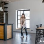 Woman mopping the floor in a contemporary kitchen and dining area with natural light.