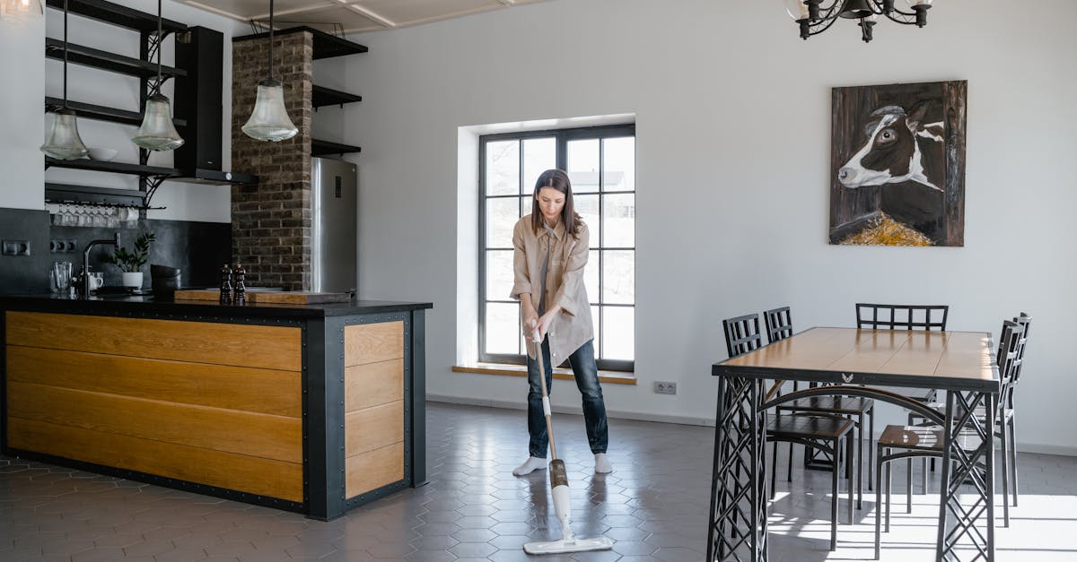 Woman mopping the floor in a contemporary kitchen and dining area with natural light.