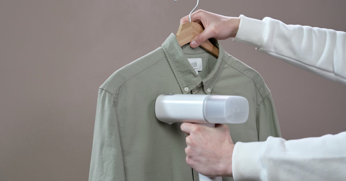 Hands steaming a green shirt with a portable steamer against a grey background.